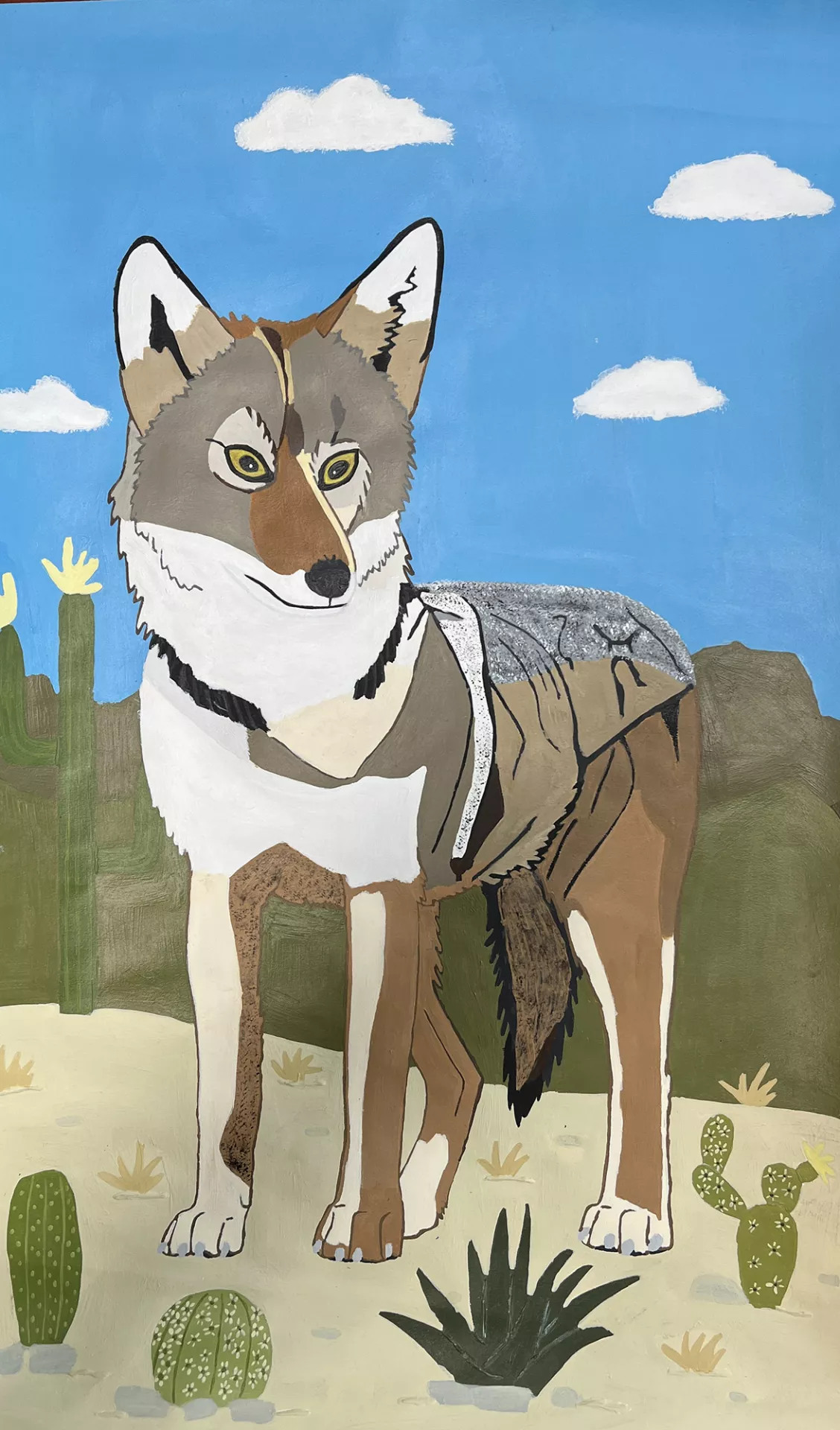 Ariana Sanchez Coyote, 2022 In this painting a coyote stands in a desert environment. The coyote is painted in browns and grays with crisp patches of various tones and textures. There are cacti around and behind the animal. The coyote faces us, its expression calm, its eyes pronounced. In the background is a blue cloudy sky. Acrylic on paper, 18” x 12”