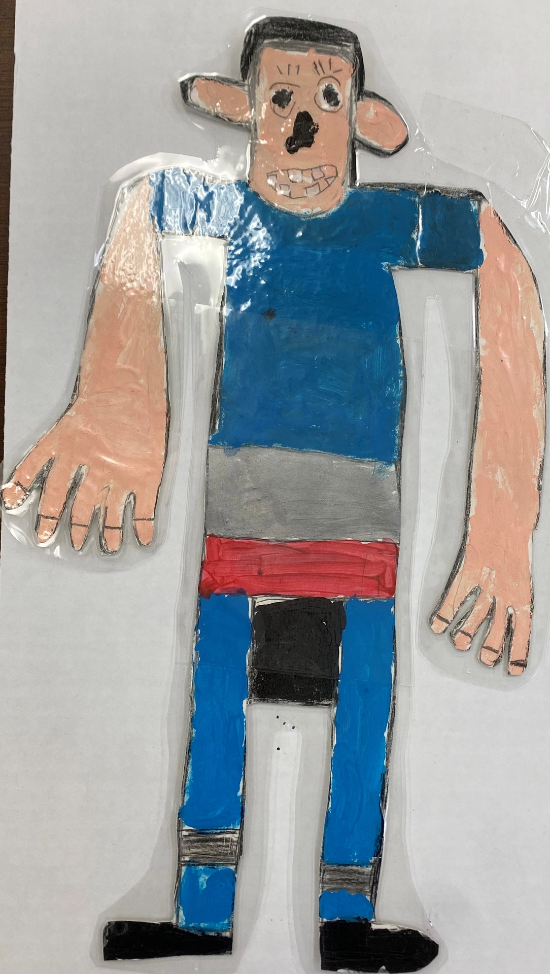 A photograph of a cutout figure of Luis with black hair, large ears, and a toothy grin. His long arms hang to his waist.