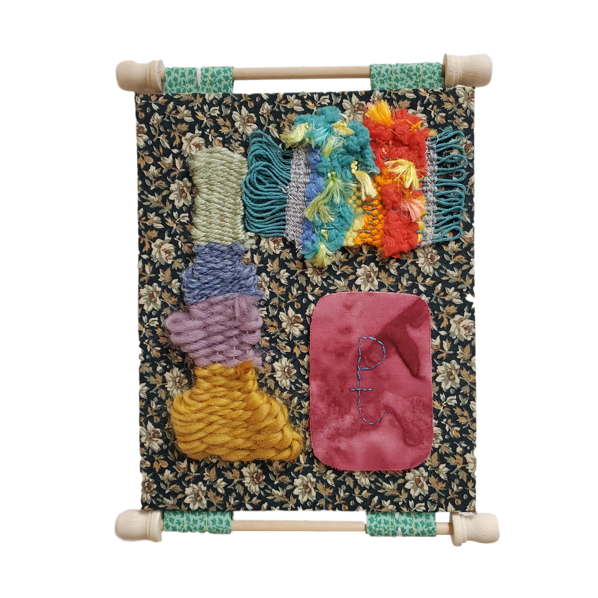 A photograph of a weaving on a white floral on dark background fabric. The weaving consists of narrow vertical and horizontal samples. The vertical sample comprises various yarns in stripes of white, purples, and yellow. The horizontal sample is comprised of various threads and yarns of blues, gray, yellow, and orange. A marbled magenta patch with a symbol representing a paradise tree is in the remaining corner of the fabric.