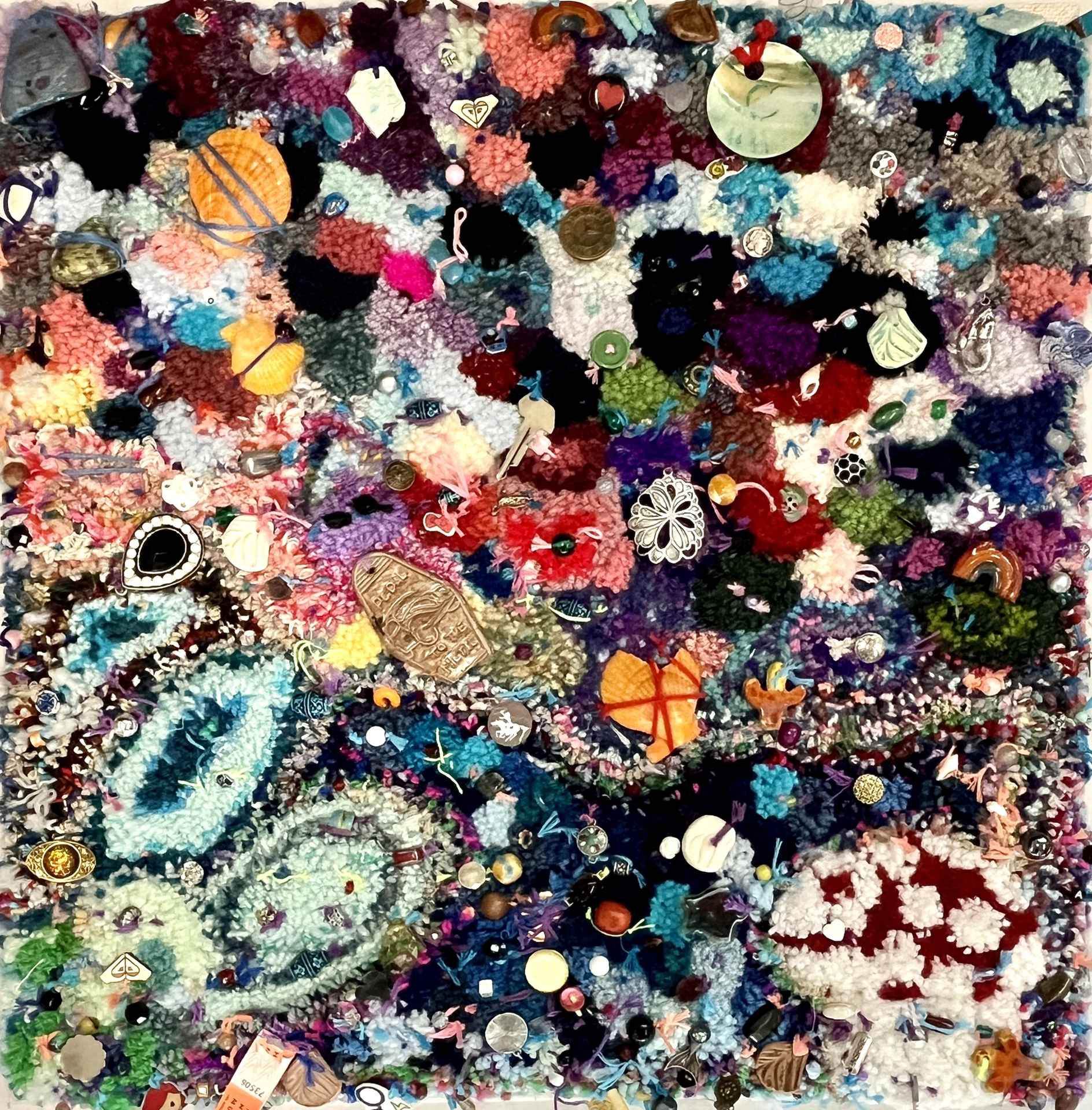 This punch needle textile is a color block composition of bold and pastel shapes. It's adorned with found objects like seashells, pendants, beads, and ceramic pieces.