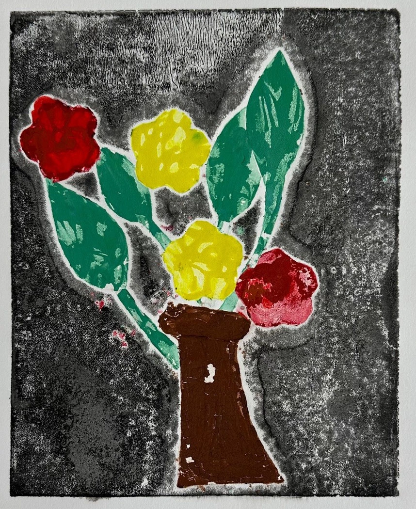 A large white border surrounds and focuses on a small picture of a brown vase that is shaped like a castle chess piece. The vase has large green leaves, and four flowers in it – two red and two yellow. These objects stand out against a black background.